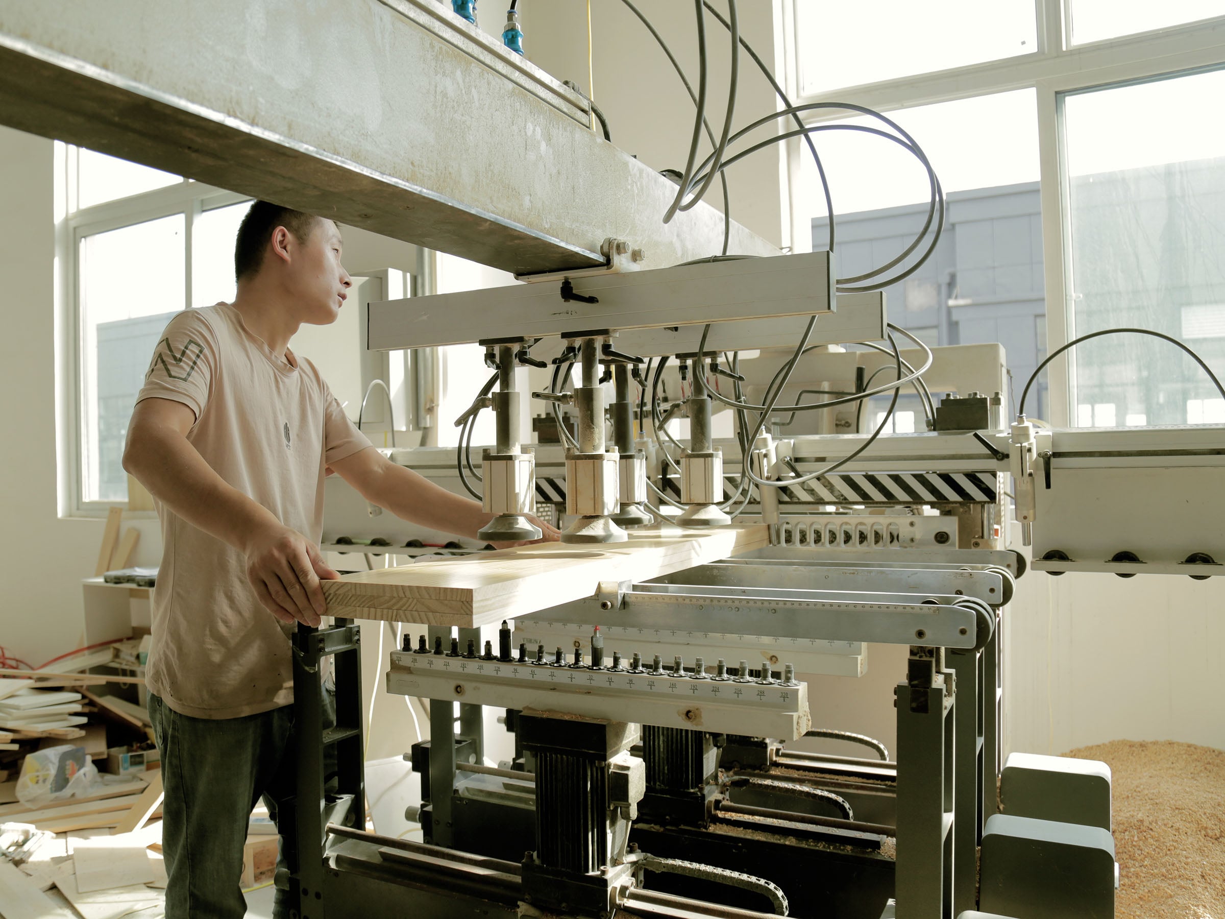 Wooden children's furniture production at MJK factory in Xuzhou, China — worker operating multi-spindle drilling machine